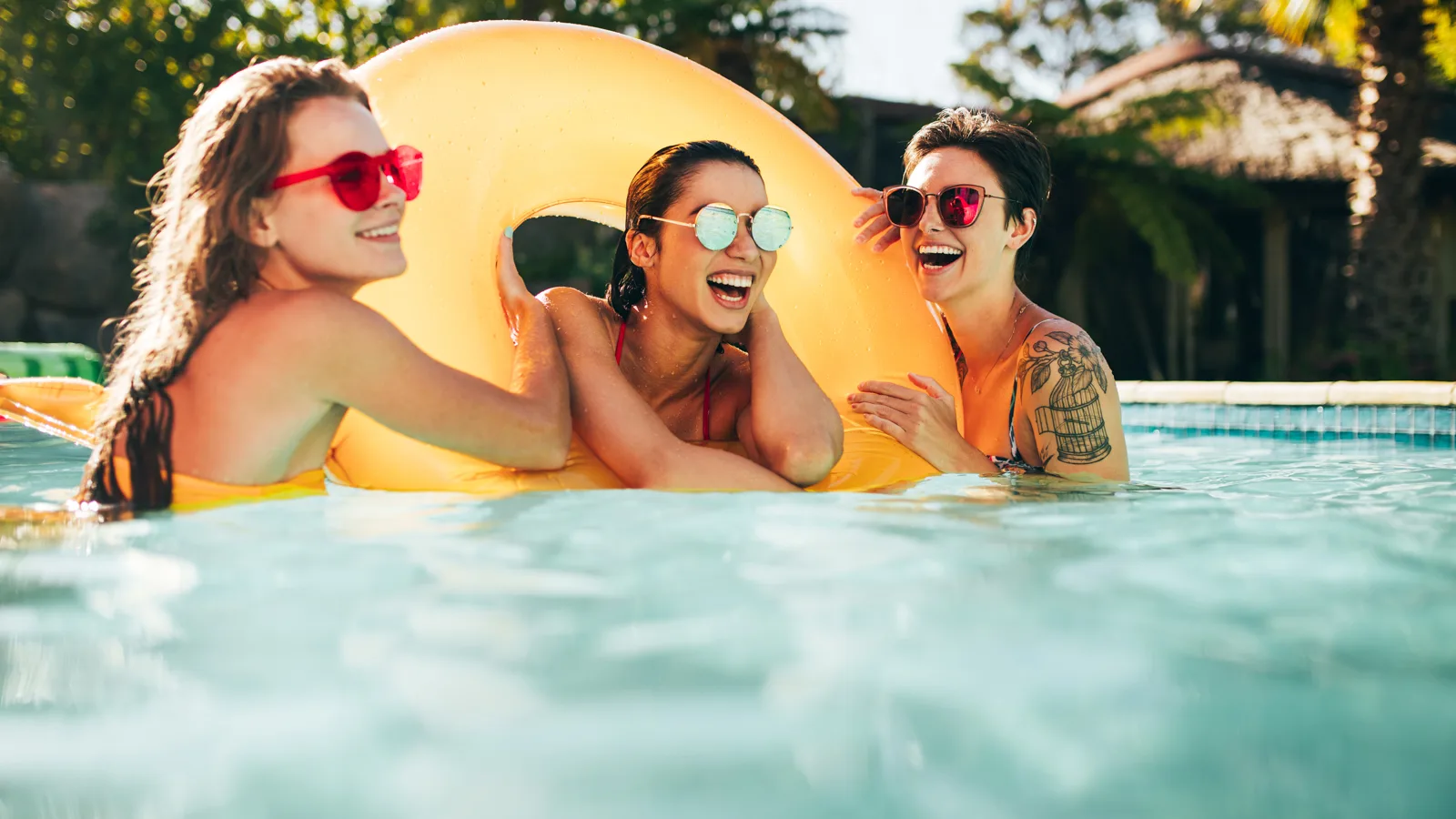 Three young women who are close friends take a selfie with a yellow ring pool float. There is one woman in the middle of the ring. She has gold sunglasses and a red bikini. The woman on the left wearing a mustard yellow swimsuit and has red sunglasses. She is holding the side of the float. The third woman is on the far right and in a blue and white abstract pattern bikini with brown sunglasses, short hair, and a left arm tattoo of a plant with flowers and a bird cage. New pet-friendly apartment homes for rent with private fenced backyards in Arizona, Texas, Florida, and North Carolina with pool, pickleball, dog park, gym, clubhouse and gated community. *No breed or weight restrictions. Yardly